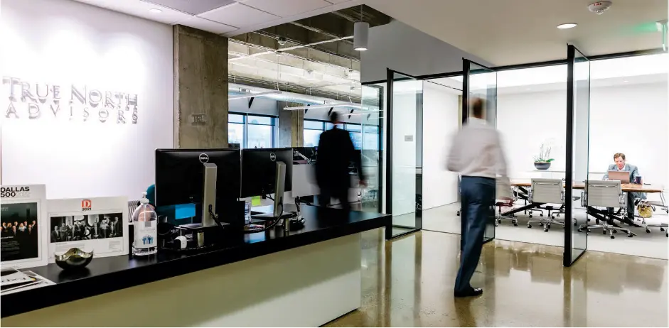 Modern office lobby of True North Advisors with glass partitions, reception desk, and employee walking through workspace.